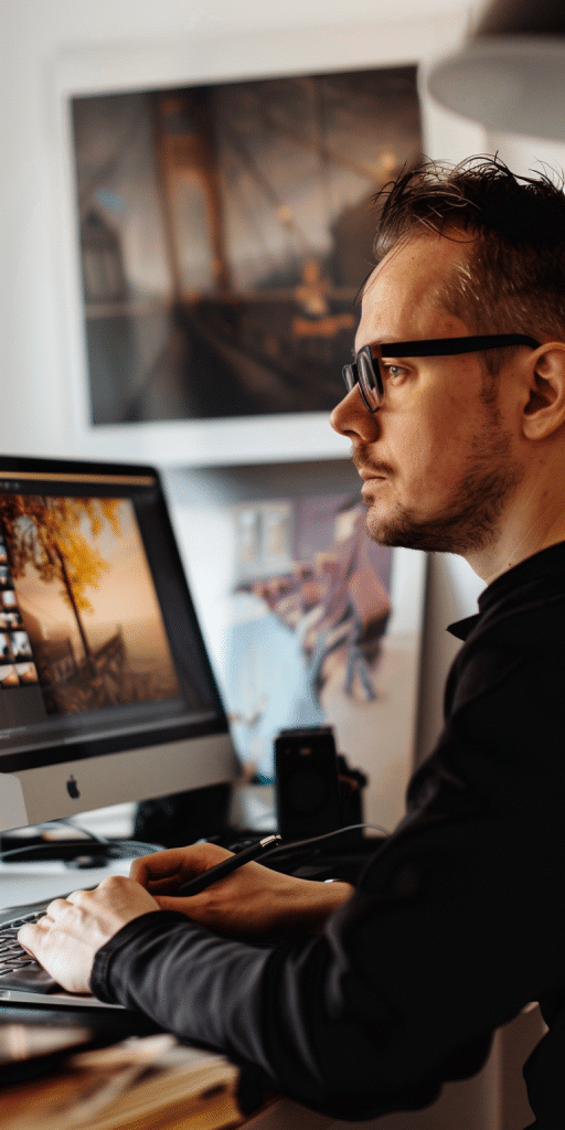Ein ernsthafter junger Mann sitzt vor einem Computer in einem modernen Büro und betrachtet aufmerksam digitale Bilder, die er gerade bearbeitet.
